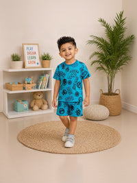 A young boy smiling and wearing a bright blue two-piece pajama set with black cartoon graphics, standing on a round woven rug in a child's bedroom.